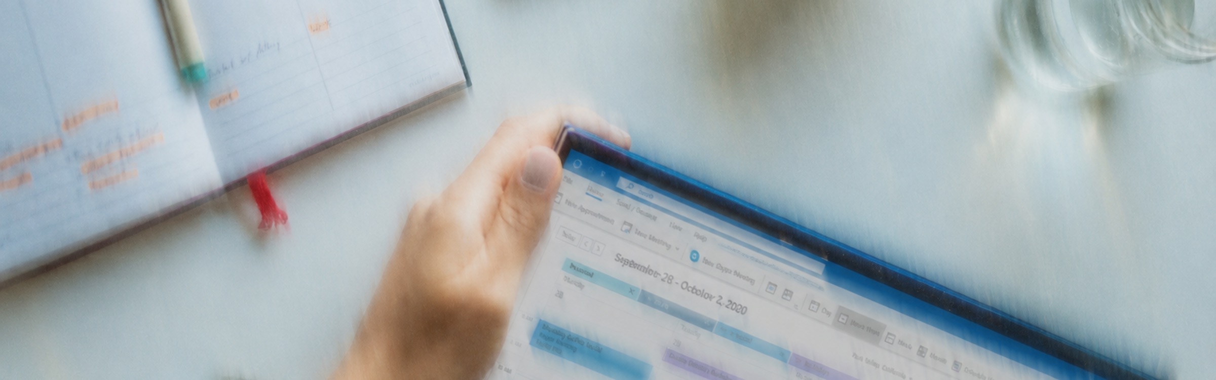 A hand holding a tablet open to a calendar, next to a planner